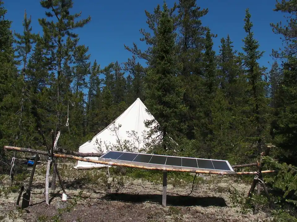 A white bell tent in a pine clearing with a solar panel mounted on a timber frame in front