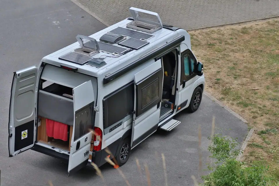 A camper van seen from above with solar panels and open roof vents on its roof, parked beside a grassy verge