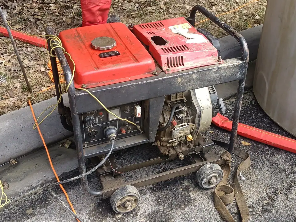 A worn red portable generator on wheels standing on pavement outdoors, with cords plugged into its panel