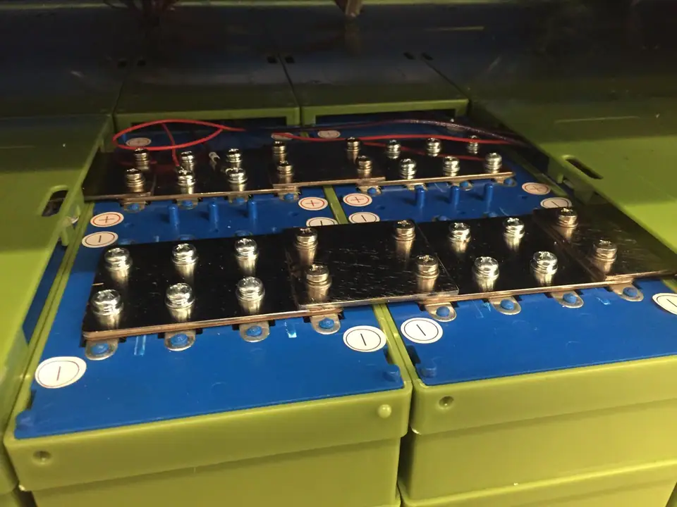 Rows of large prismatic lithium iron phosphate cells joined by metal busbars in a battery pack