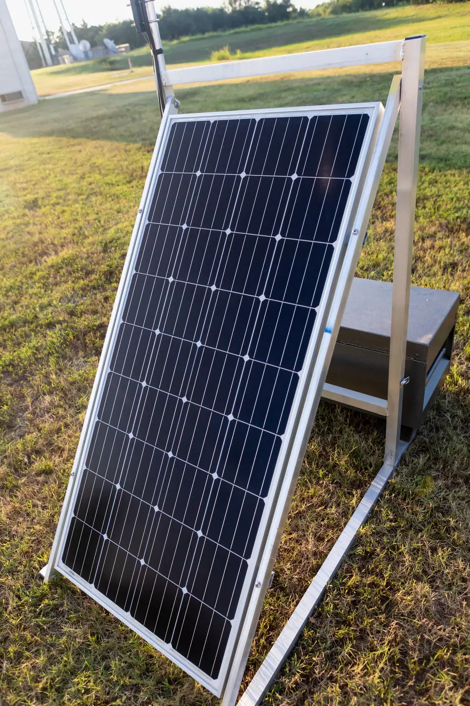 A single solar panel on an aluminum stand in the grass, angled toward the sun