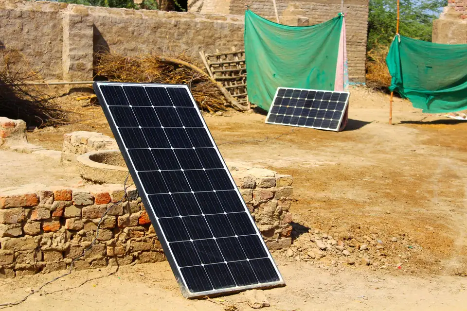 Two solar panels leaning in the sun against a low stone wall in a dirt courtyard