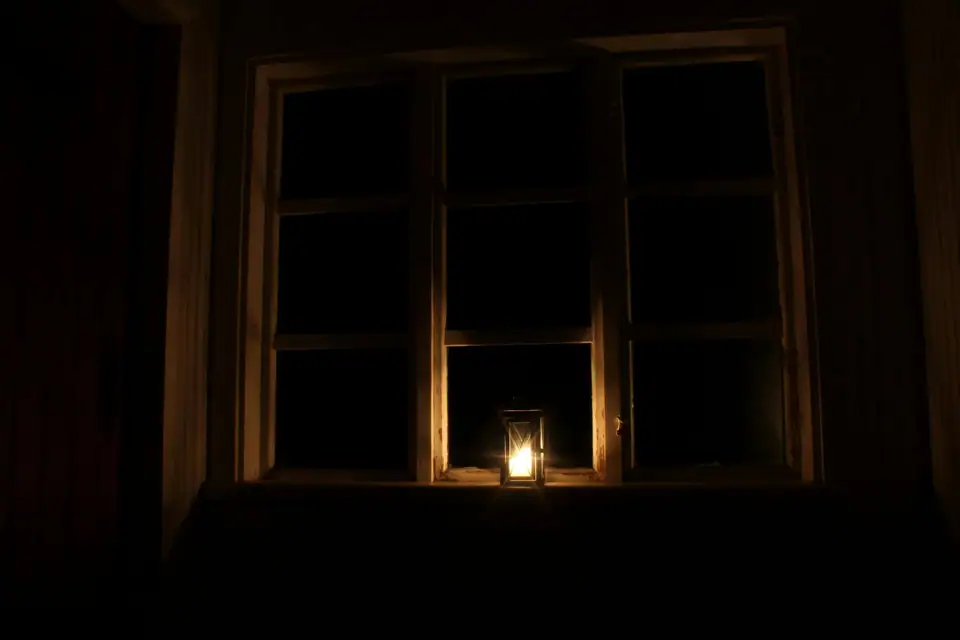 A candle lantern glowing on the sill of a dark window at night